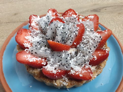 une tartelette de fraises avec fruits du dragon et noix de coco sur une assiette bleu sur une table en bois